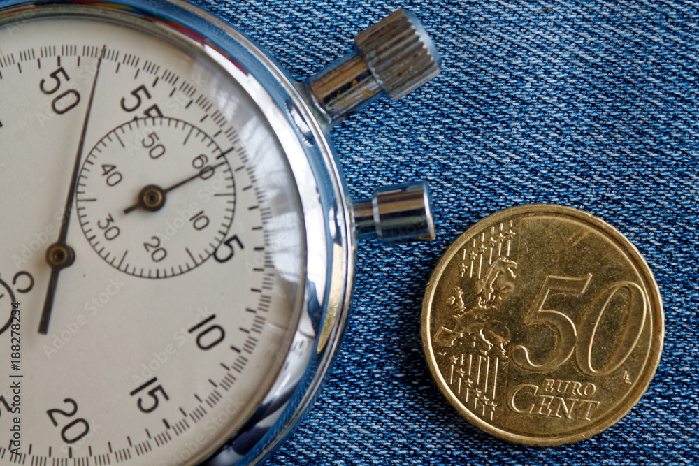 Euro coin with a denomination of 50 euro cents and stopwatch on worn blue denim backdrop - business background