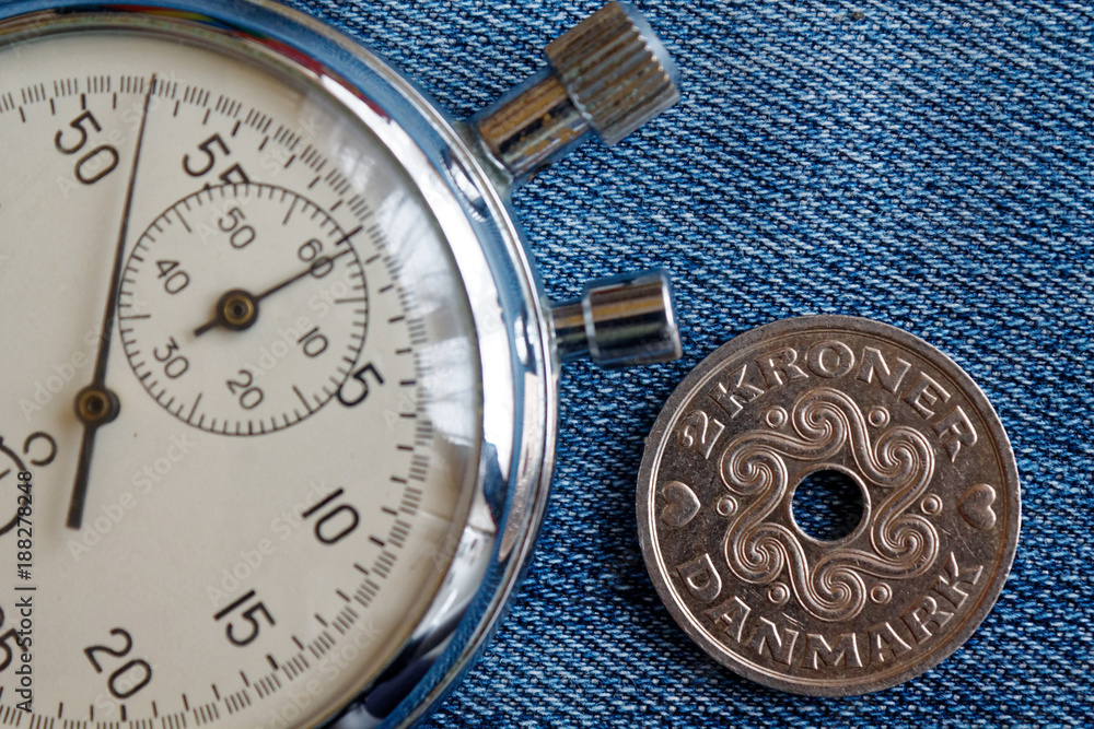 Denmark coin with a denomination of 2 krone (crown) and stopwatch on worn blue denim backdrop - business background