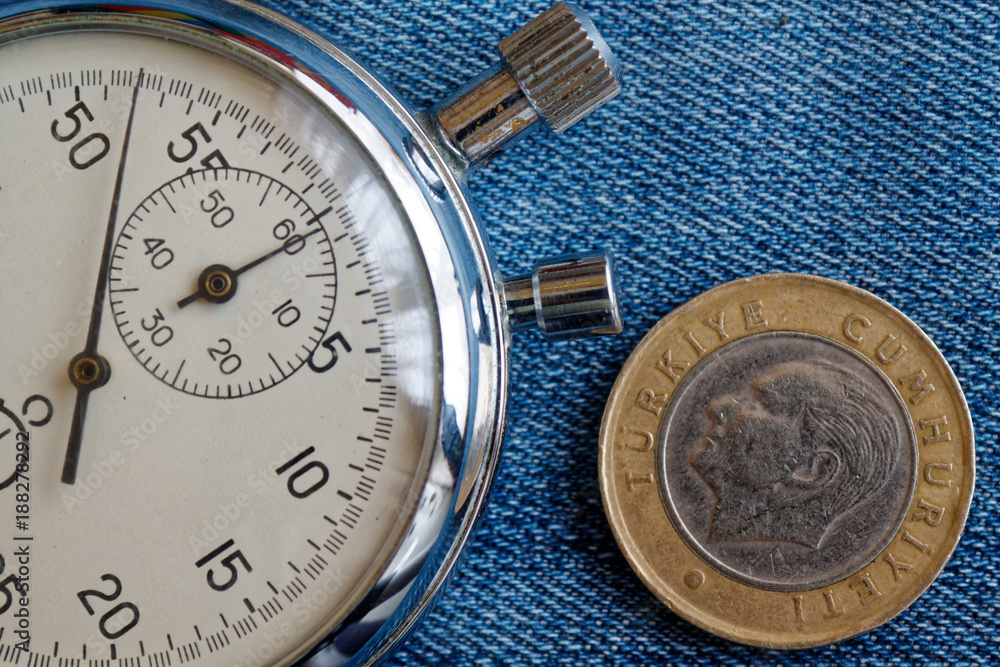 Turkish coin with a denomination of one lira (back side) and stopwatch on worn blue jeans backdrop - business background