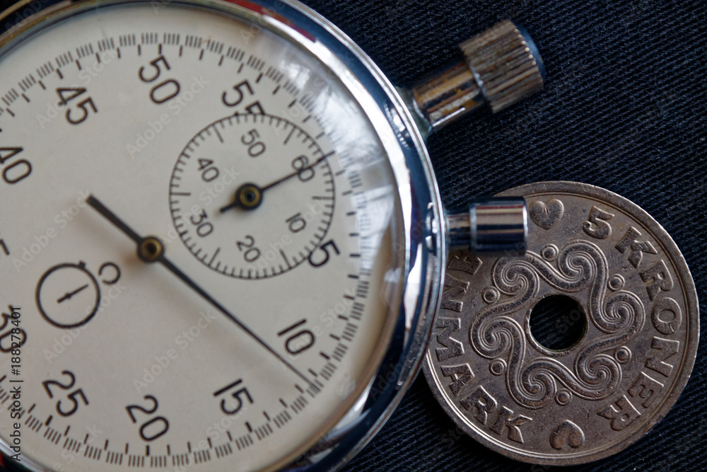 Denmark coin with a denomination of 5 krone (crown) and stopwatch on black denim backdrop - business background Denmark coin with a denomination of 5 krone (crown) and stopwatch on black denim backdrop - business background