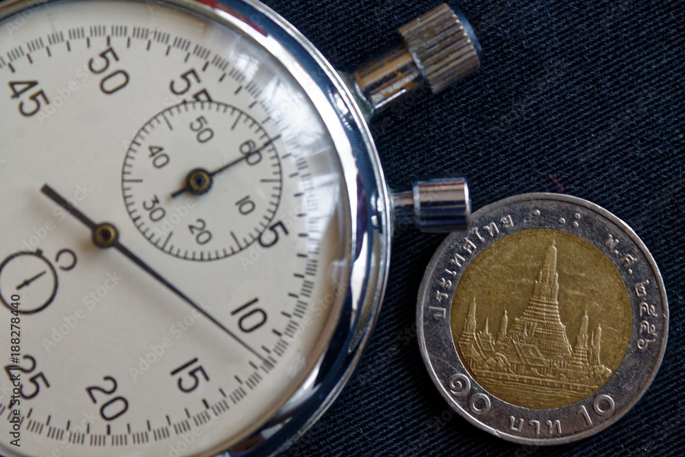 Thai coin with a denomination of 10 baht and stopwatch on old worn black jeans backdrop - business background Thai coin with a denomination of 10 baht and stopwatch on old worn black jeans backdrop - business background