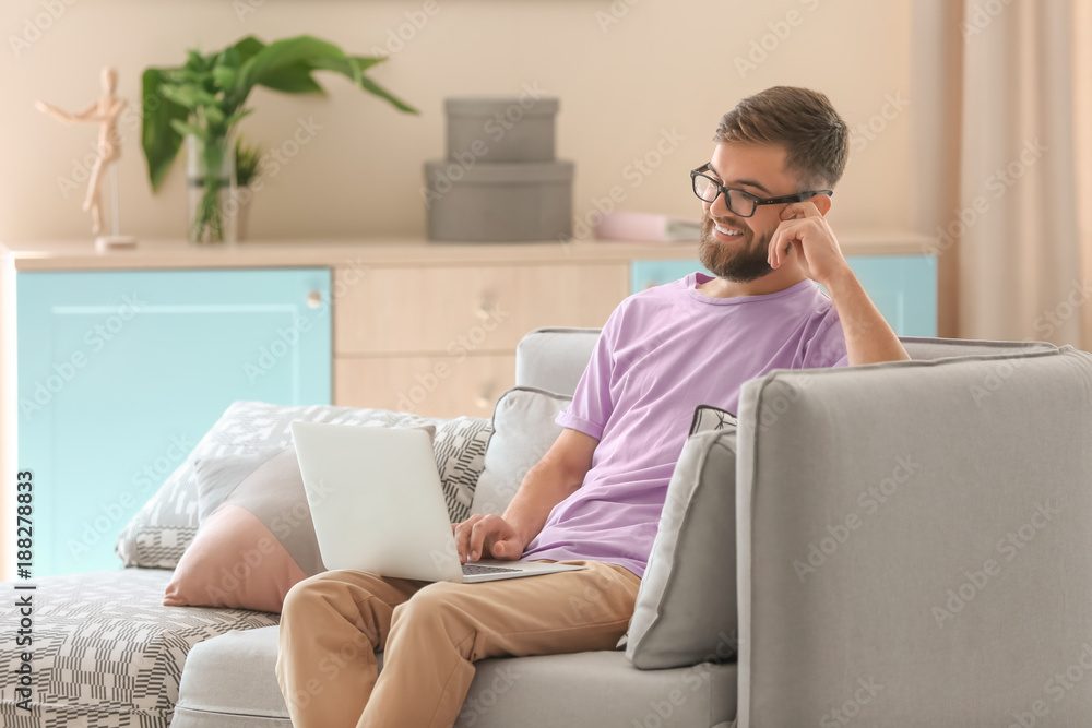 Naklejka premium Young man using his laptop while sitting on sofa indoors
