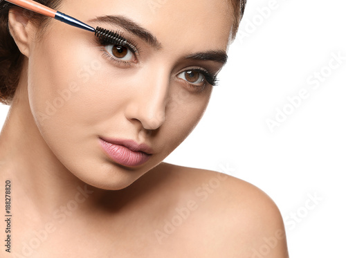 Beautiful young woman with eyelash extensions applying mascara, on white background