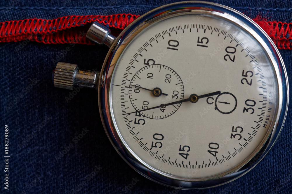 Stopwatch on dark blue denim background with red strip, value measure time, old clock arrow minute and second accuracy timer record Stopwatch on dark blue denim background with red strip, value measure time, old clock arrow minute and second accuracy timer record