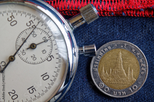 Thai coin with a denomination of 10 baht and stopwatch on old worn dark blue jeans with red stripe backdrop - business background