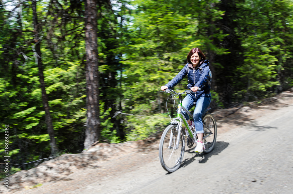 Smiling Woman Riding a Bicycle on an Unpaved Road through a Forest on a Sunny Spring Day. Blurred Motion.