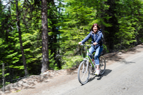 Smiling Woman Riding a Bicycle on an Unpaved Road through a Forest on a Sunny Spring Day. Blurred Motion.