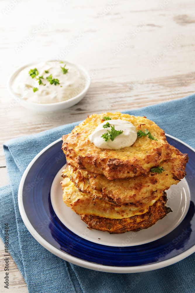 golden fried rosti pile from cauliflower and parmesan cheese with a creamy dip and parsley garnish, blue napkin, bright wooden table with copy space, vertical golden fried rosti pile from cauliflower and parmesan cheese with a creamy dip and parsley garnish, blue napkin, bright wooden table with copy space, vertical