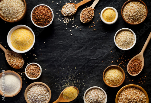 Various groats, cereals. Different types of groats in bowls and on a spoons on a  black background, top view. Healthy nutrition food