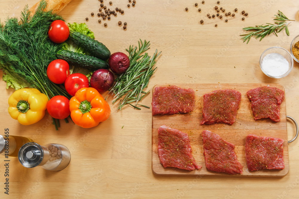 Raw meat. Pieces fresh beef, lamb or pork tenderloin on cutting board on wooden table with different vegetables, spices, mushrooms, baking tray, knife. Top view flat lay. Copy space for advertisement. Raw meat. Pieces fresh beef, lamb or pork tenderloin on cutting board on wooden table with different vegetables, spices, mushrooms, baking tray, knife. Top view flat lay. Copy space for advertisement.