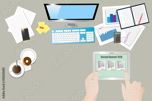 Top view of the office workplace with hands  holding tablet with a calendar for second quarter of 2018 year on the screen
