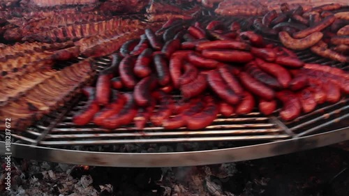 Parrilla girando con carnes asadas al aire libre. Carnes de cerdo, chorizos, salchichas y longanizas