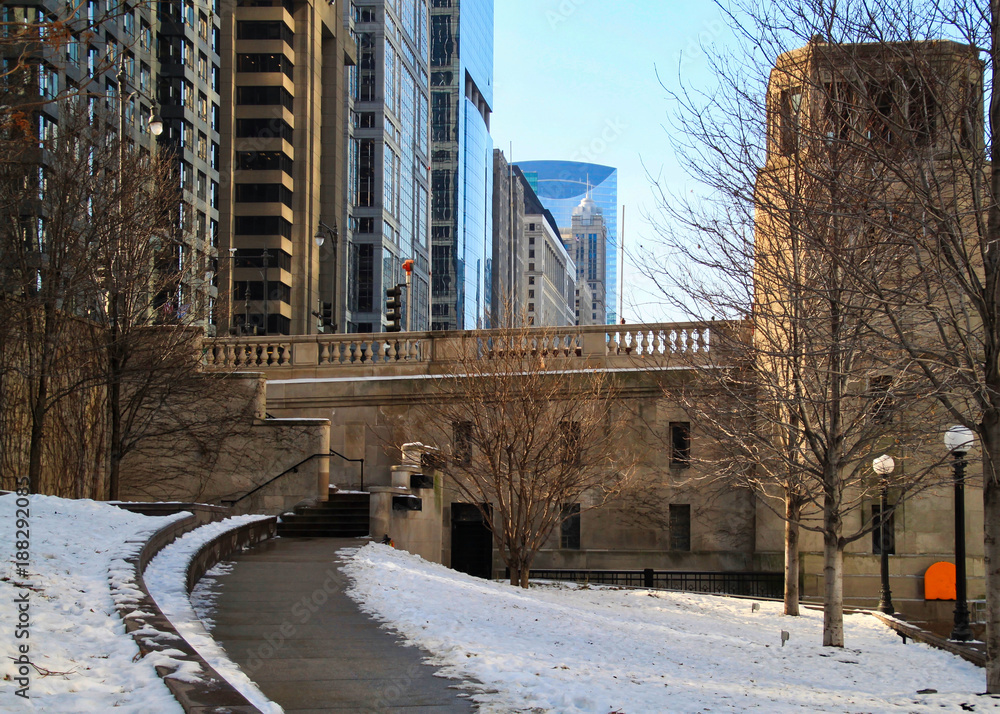 Path along Chicago riverwalk during winter midday with snow piles.