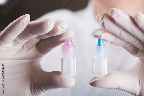 Hands in medical gloves holding two different plastic bottles with laboratory reagents