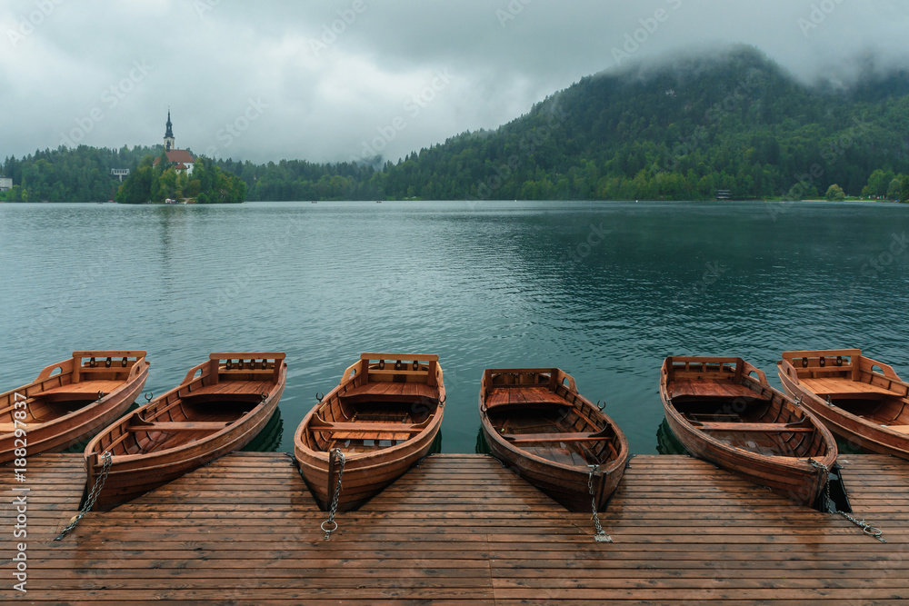 Bled with lake, island, castle, boats and mountains in background in misty and rainy day, Slovenia