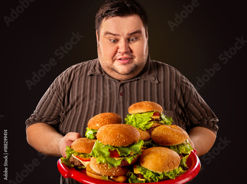 Diet failure of fat man eating fast food. Happy smile overweight person who crazy makes squint for fun eating huge hamburger on fork. Food is main thing in life. Man suffers from gluttony.