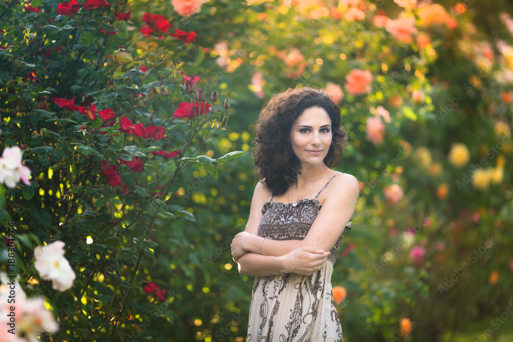 A young woman with curly hair in a rose garden A young woman with curly hair in a rose garden