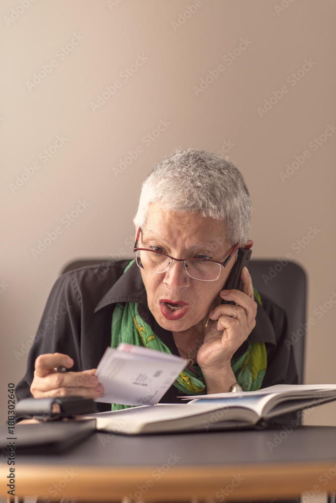 Shocked senior woman raging on her cell phone over her pricey electricity bills