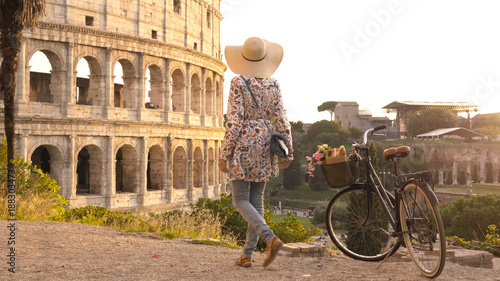 Photography Young woman tourist with bycicle takes pictures of the colosseum in rome at sunset with smartphone