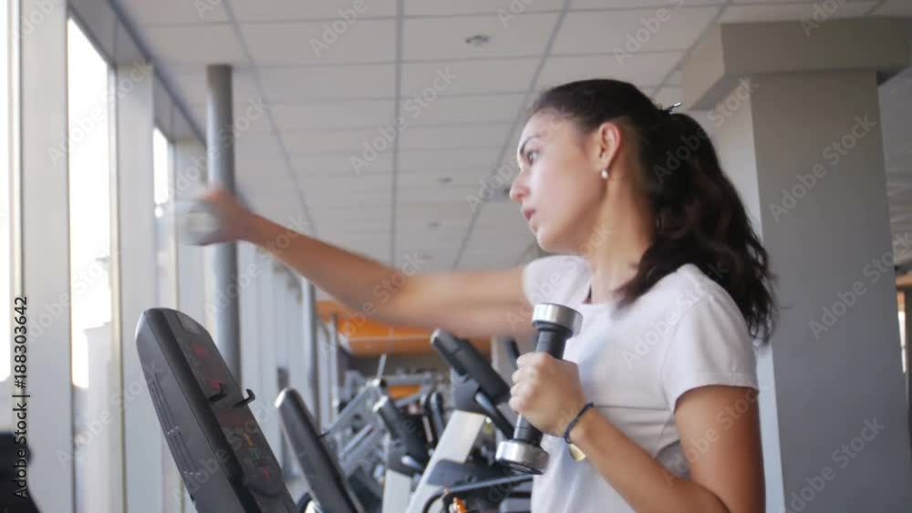 beautiful young girl woman with dumbbells running on a treadmill beautiful young girl woman with dumbbells running on a treadmill