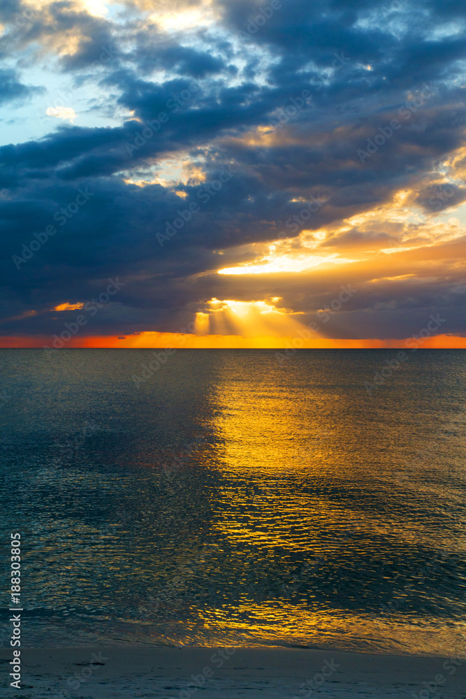 Amazing epic seascape of colorful sunset view from sandy beach, bright sunbeam rays of warm sun light transect the dark cloudy sky above blue sea Amazing epic seascape of colorful sunset view from sandy beach, bright sunbeam rays of warm sun light transect the dark cloudy sky above blue sea