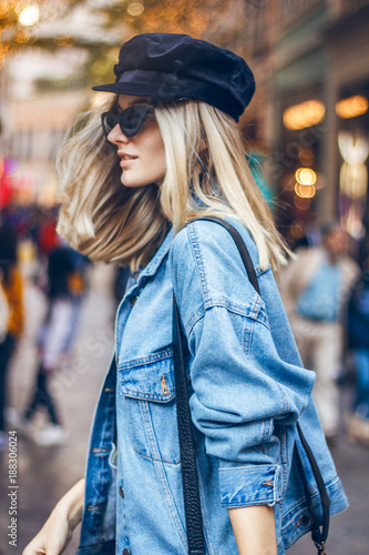 Portrait of a beautiful young blond woman with fashionable black sunglasses walking through street in Hong Kong. She is dressed in black clothes with a denim jacket and dancing on the street.