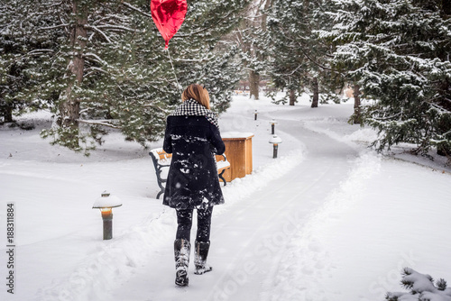 Fototapeta Naklejka Na Ścianę i Meble -  woman walking in the woods on a snowy day holding red heart shaped balloon