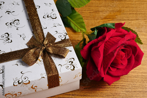 White gift box with red rose on wooden background. Concept of Valentine Day.