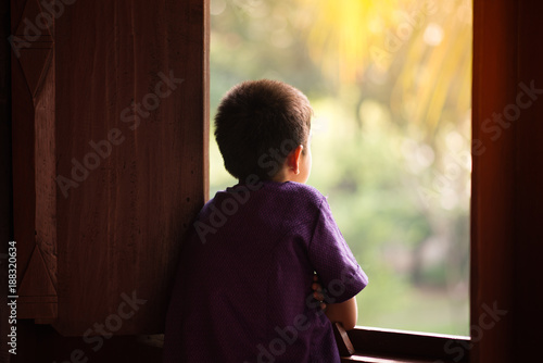 Little boy standing alone looking out of the window photo