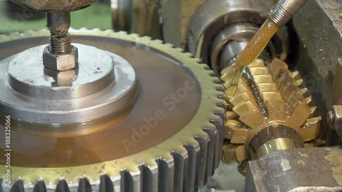 Close-up mechanism makes vertical grooves in pinion with oil. Jet of cooling yellow liquid polishes parts that are manufactured in a slow process in plant. photo