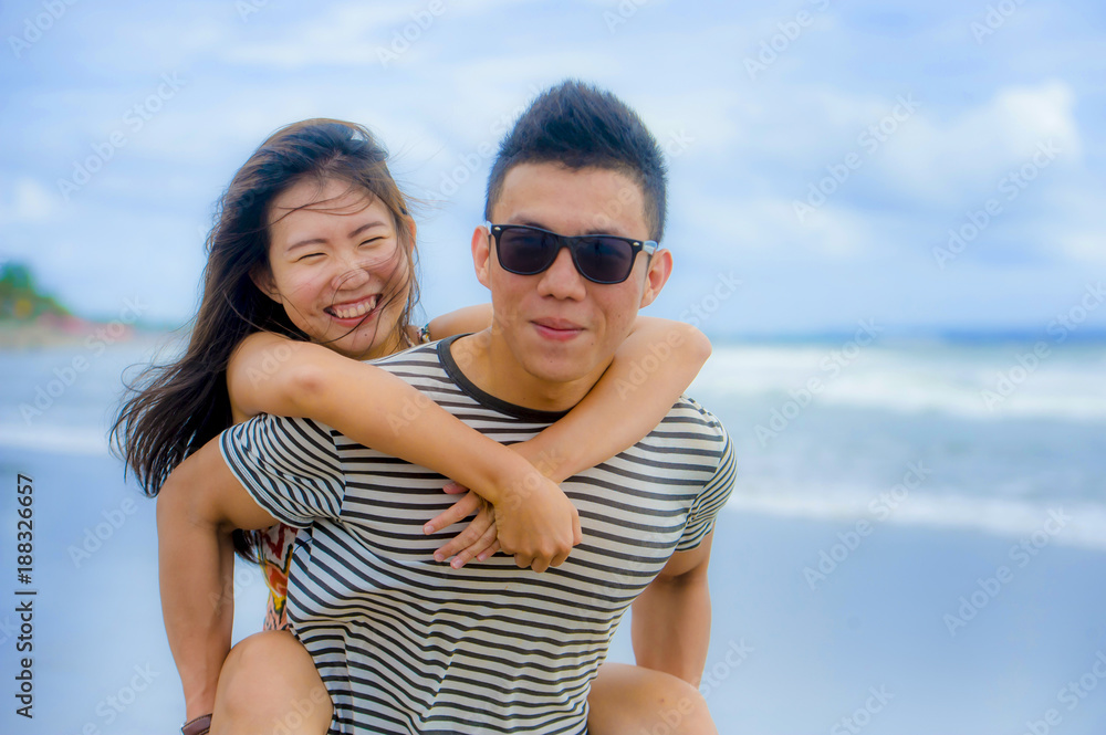 beautiful Asian Chinese couple with boyfriend carrying woman on her back and shoulders at the beach smiling happy in love enjoying holidays beautiful Asian Chinese couple with boyfriend carrying woman on her back and shoulders at the beach smiling happy in love enjoying holidays