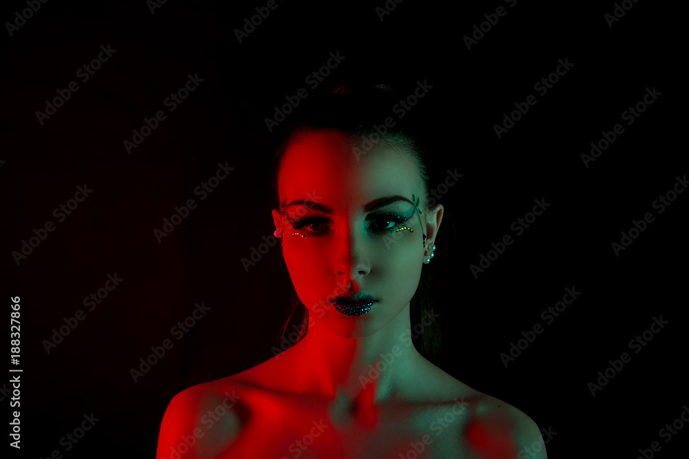 Brunette girl with red and green illumination on the face against a black background closeup Brunette girl with red and green illumination on the face against a black background closeup