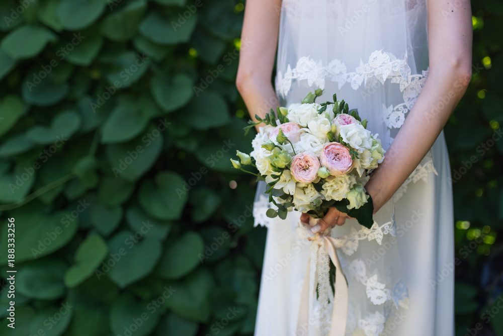 Bride holds in her hands wedding bouquet with pink and white roses on a greenery background Bride holds in her hands wedding bouquet with pink and white roses on a greenery background