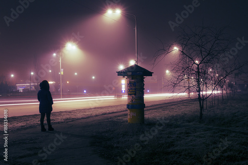 Fototapeta Naklejka Na Ścianę i Meble -  A lonely woman walking along the night street, lit by street lights and car headlights.