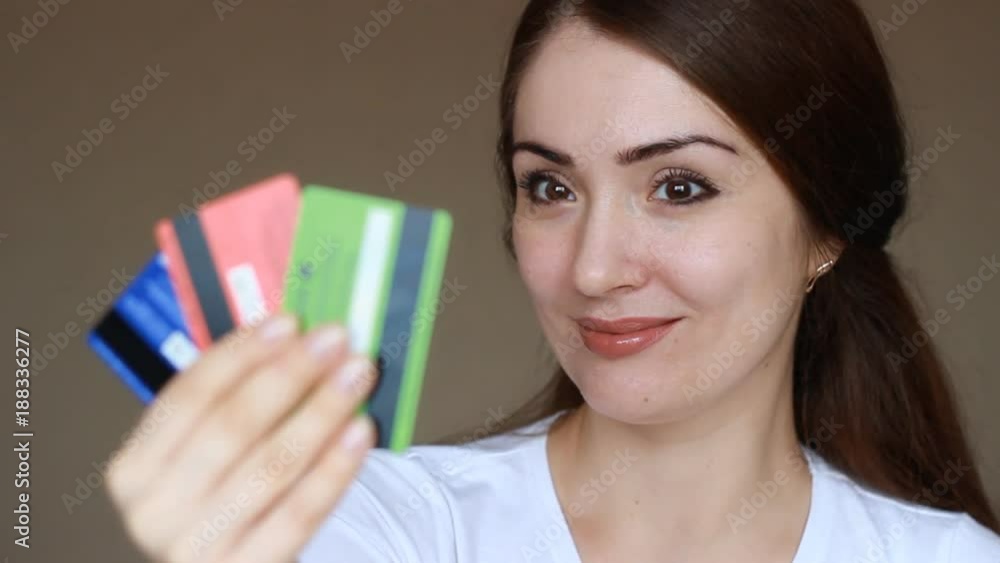 Portrait of a young beautiful woman close-up, who is smiling, looking at the camera and holding credit bank cards of different colors and banks. The concept of choosing and saving credit, finance, and Portrait of a young beautiful woman close-up, who is smiling, looking at the camera and holding credit bank cards of different colors and banks. The concept of choosing and saving credit, finance, and