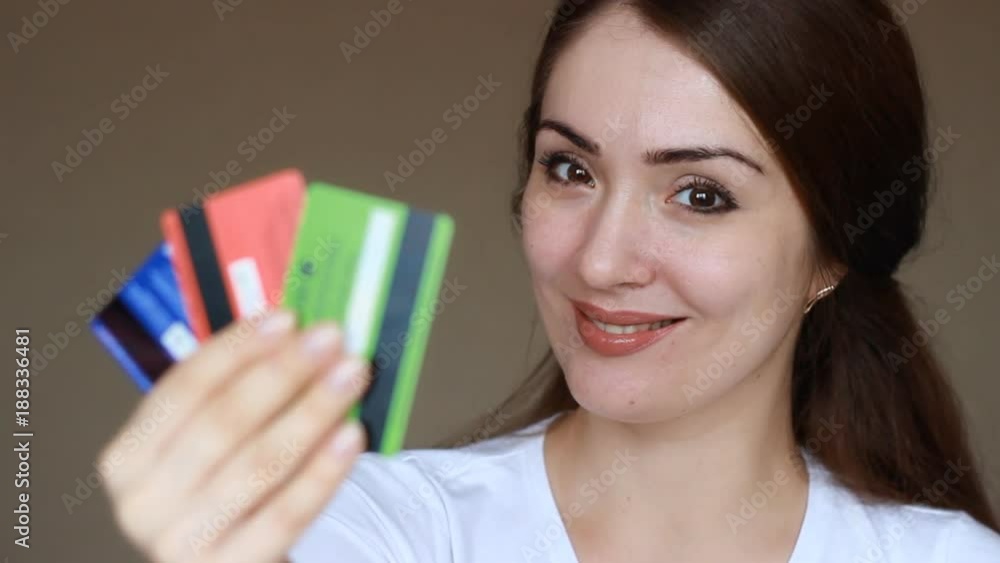 Portrait of a young beautiful woman close-up, who is smiling, looking at the camera and holding credit bank cards of different colors and banks. The concept of choosing and saving credit, finance, and Portrait of a young beautiful woman close-up, who is smiling, looking at the camera and holding credit bank cards of different colors and banks. The concept of choosing and saving credit, finance, and