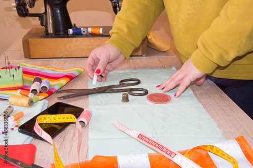 Seamstress hands on the work table with pattern and measuring tape. A tailor is laying out a dress