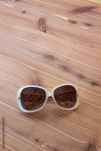 Mod vintage frame on woman sunglasses, white with mod sides, rhinestones, on wood background, copy space, vertical aspect