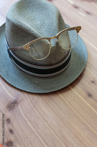 Vintage hipster concept with retro fedora hat, metal horn rimmed glasses perched on the front, neutral wood background, copy space, vertical aspect