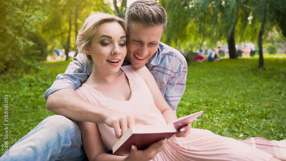 Couple of students in love sitting on rug reading educational book together Couple of students in love sitting on rug reading educational book together