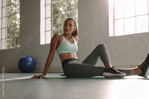 Female athlete sitting on exercise mat at fitness club