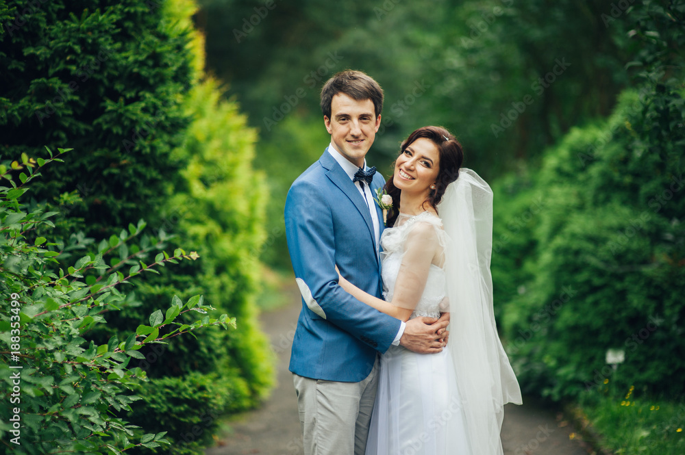 Happy smiling stylish bride and groom walking in the summer gree