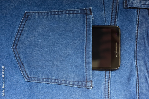 Black smart mobile phone in back blue jeans pocket denim background texture.