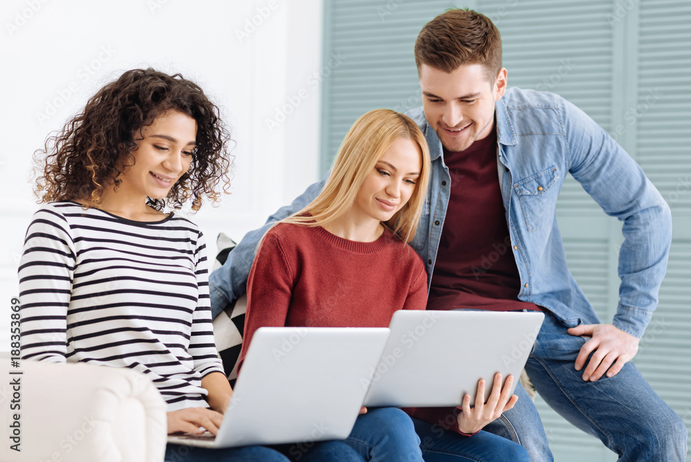 Team work. Handsome brunette man keeping smile on his face and sitting near his friend while watching video