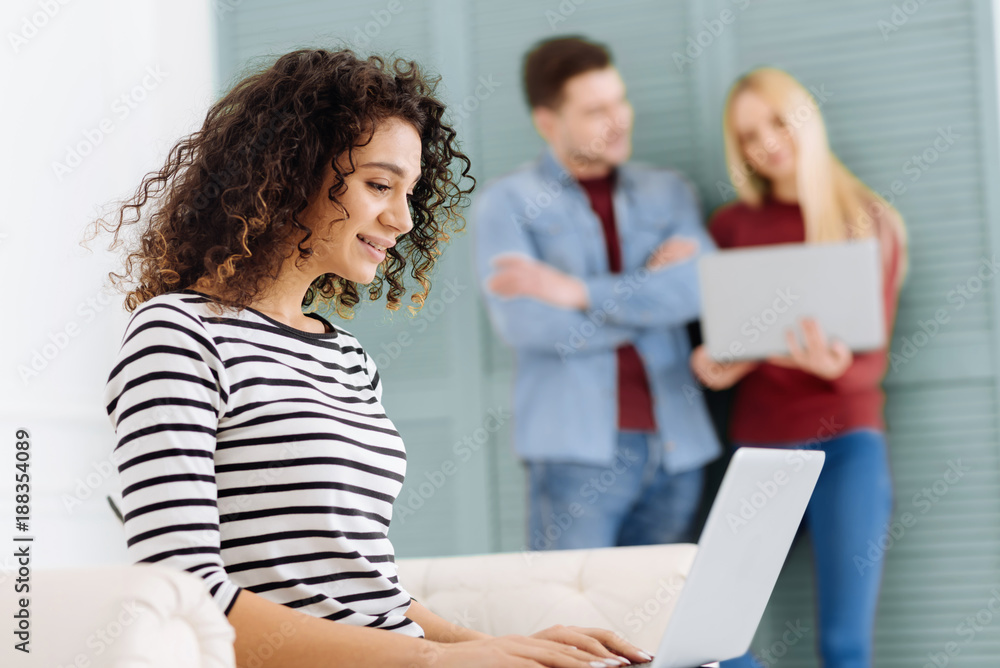 Online communication. Attractive girl keeping smile on her face and holding computer on knees while being on the foreground Online communication. Attractive girl keeping smile on her face and holding computer on knees while being on the foreground
