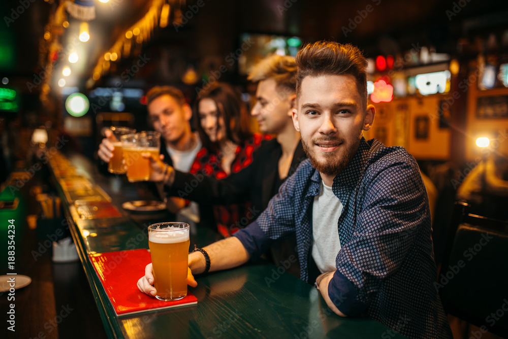 Young man holds glass with beer at the bar counter