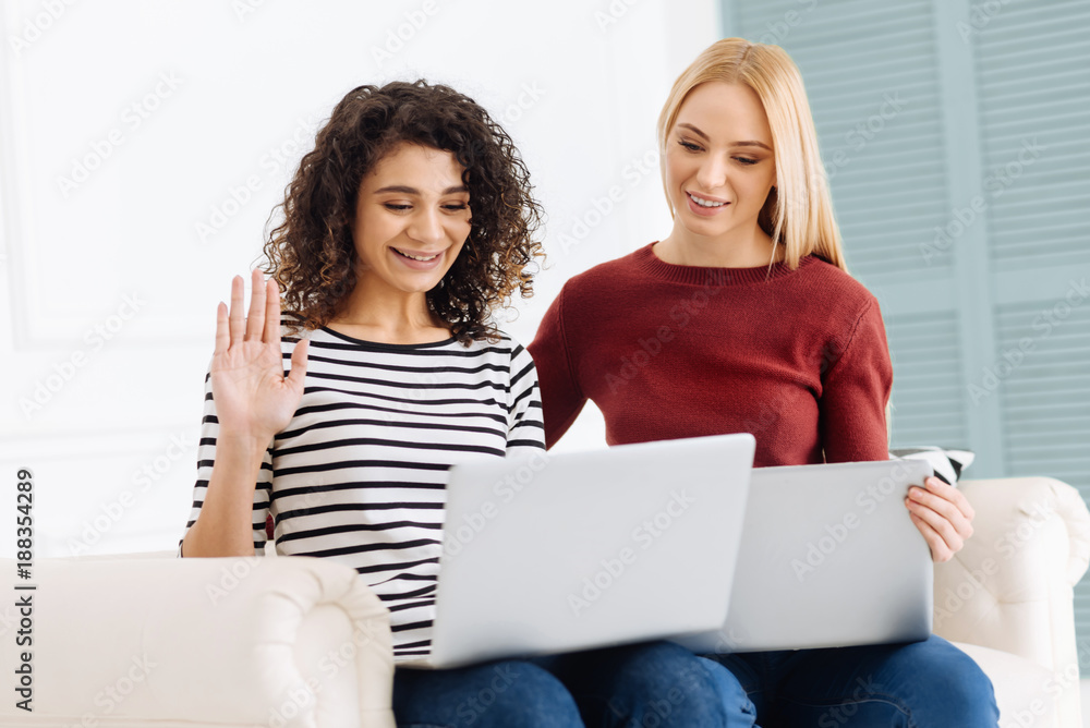 Keep smiling. Two girls expressing positivity and looking at computer while sitting on the sofa Keep smiling. Two girls expressing positivity and looking at computer while sitting on the sofa