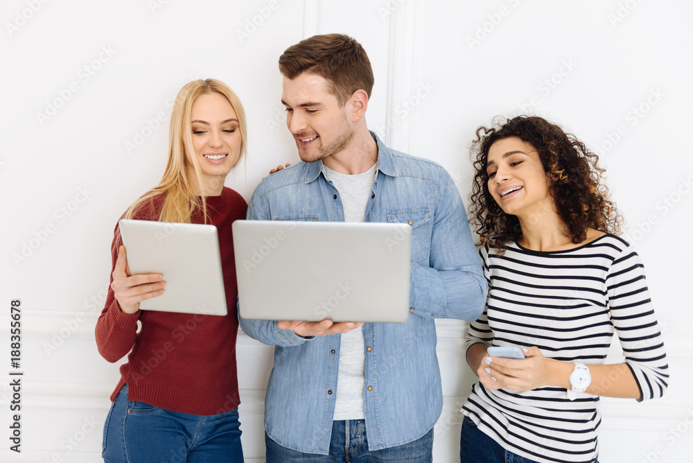 Lets compare. Cheerful blonde expressing positivity and standing near her colleague while demonstrating her tablet Lets compare. Cheerful blonde expressing positivity and standing near her colleague while demonstrating her tablet