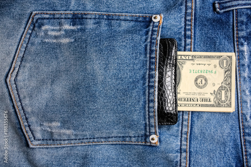 Black leather wallet with money in back blue jeans pocket denim background texture.