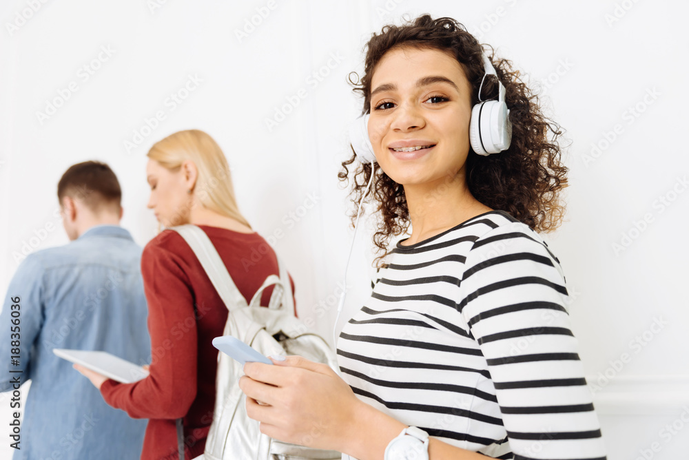 Music lover. Charming female person holding her telephone while choosing track, wearing headphones Music lover. Charming female person holding her telephone while choosing track, wearing headphones